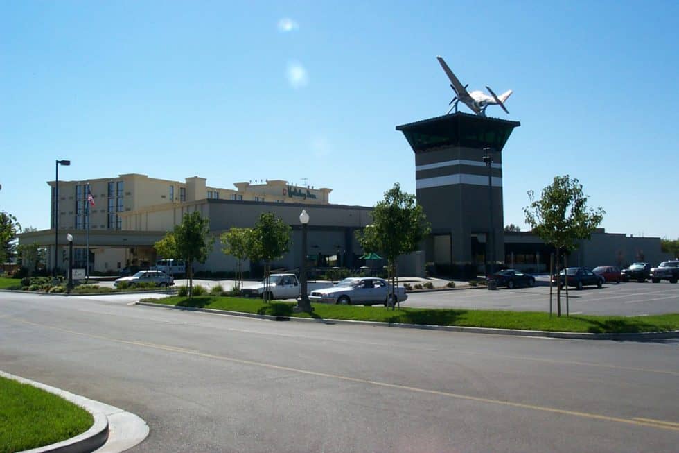 Modern shopping mall exterior featuring a prominent airplane sculpture on the tower, parking lot, and well-maintained landscaping. Perfect for retail, dining, and entertainment experiences.