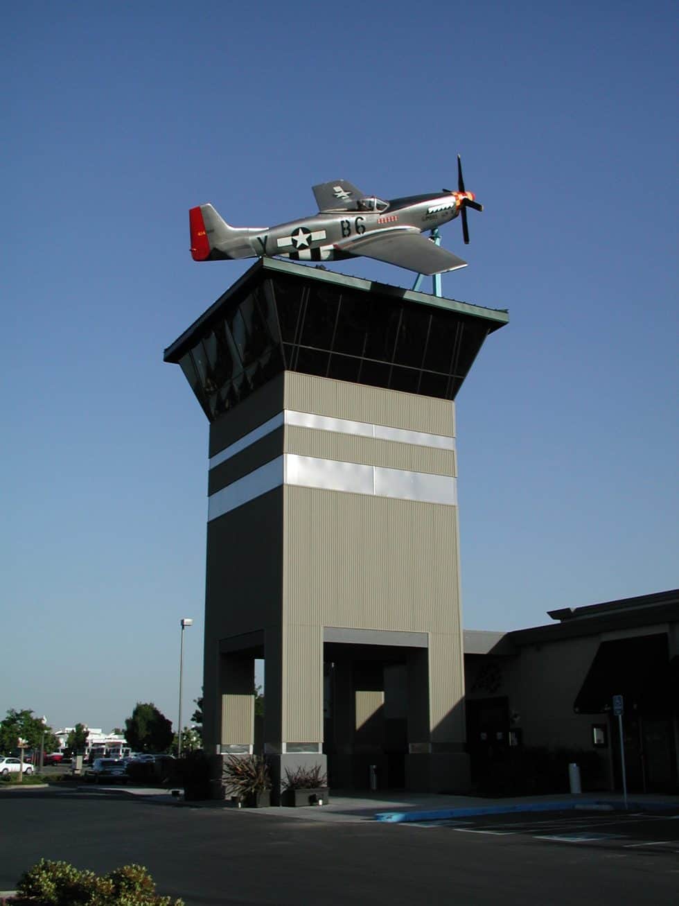 Military aircraft monument on a tall, modern control tower structure with a clear blue sky background.