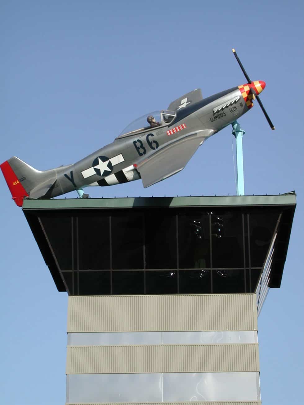 Vintage P-51 Mustang aircraft sculpture atop a modern building display, highlighting aviation art and architectural design by Lauren Anderson Design.